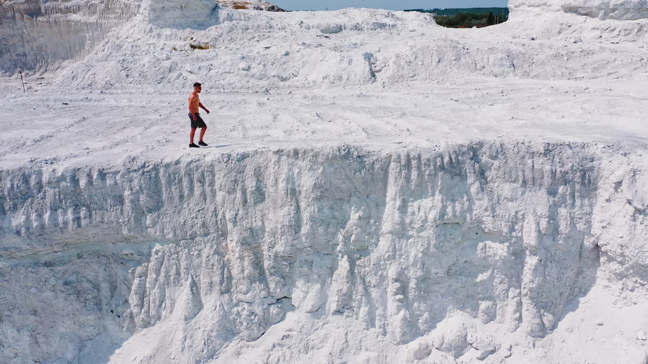 Young sporty man in white mountains. Healthy man without shirt walking along rocky canyon in a warm sunny day. Aerial view.