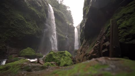 a wide, panoramic video frame reveals two magnificent waterfalls cascading down a lush, moss-covered gorge