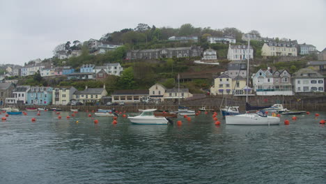 looe hillside waterfront homes overlook sailboats moored in harbour, south coast cornwall, united kingdom, wide shot