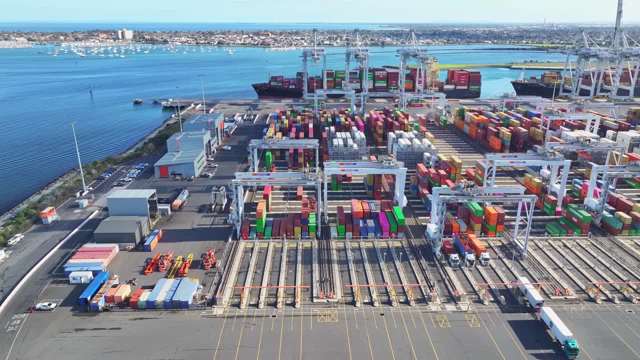 Container yard with cranes trucks and ships at Port Melbourne along waterfront harbour edge