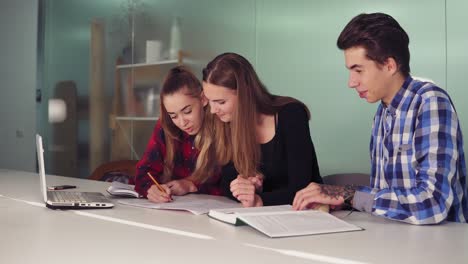 estudiantes concentrados trabajando en sus tareas sentados juntos en la mesa y bebiendo café. grupo de jóvenes en la reunión en un apartamento moderno. slowmotion tiro