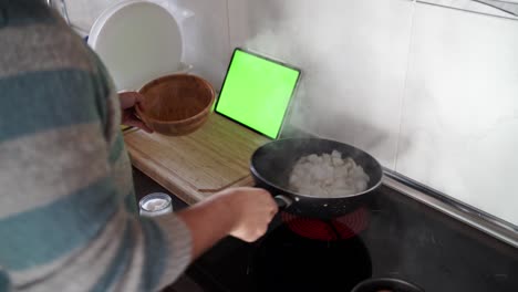 over the shoulder shot of a man cooking sepia using a recipe from his tablet