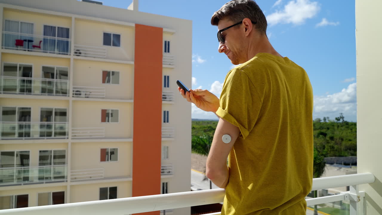 hombre adulto joven caminando hacia la barandilla del hotel y comprobando los niveles de diabetes en el brazo izquierdo con el sensor freestyle libre 2