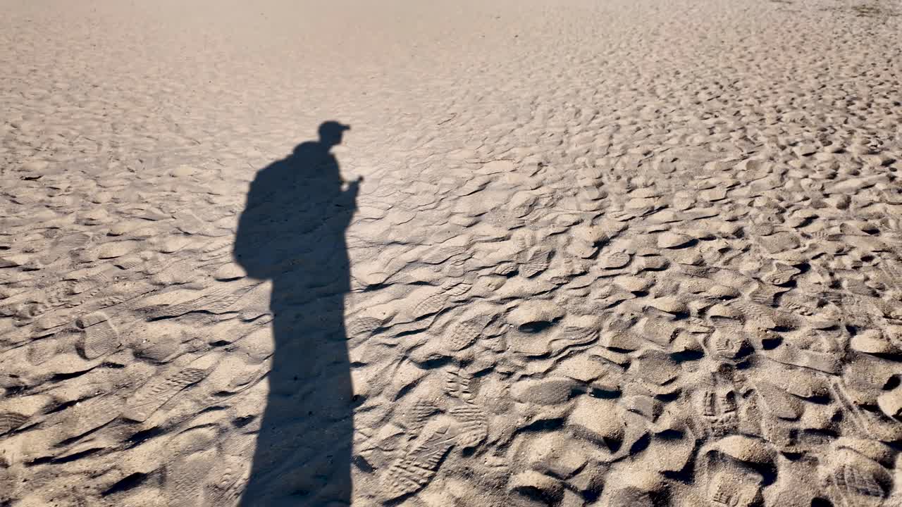 Shadow of photographer walking along Amanohashidate beach in Japan, leaving footprints in the sand