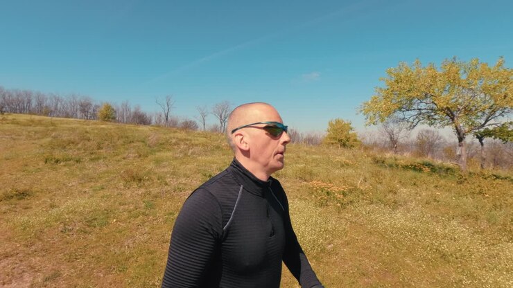 Close up shot of a mature man in his 50s running in nature. Focus on his face, sunglasses, and emotions during an active outdoor jogging session on a sunny day