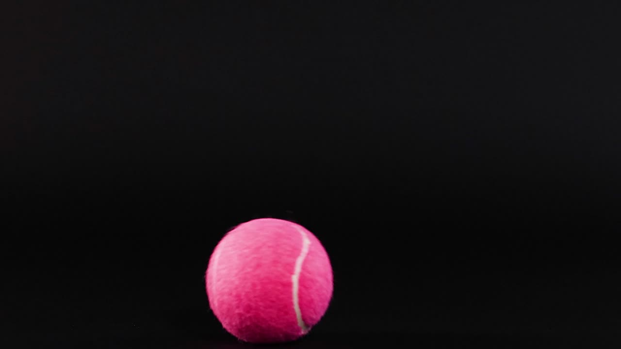 A pink tennis ball progresses across a segmented black grid, showcasing motion and contrast in a minimalist setting.