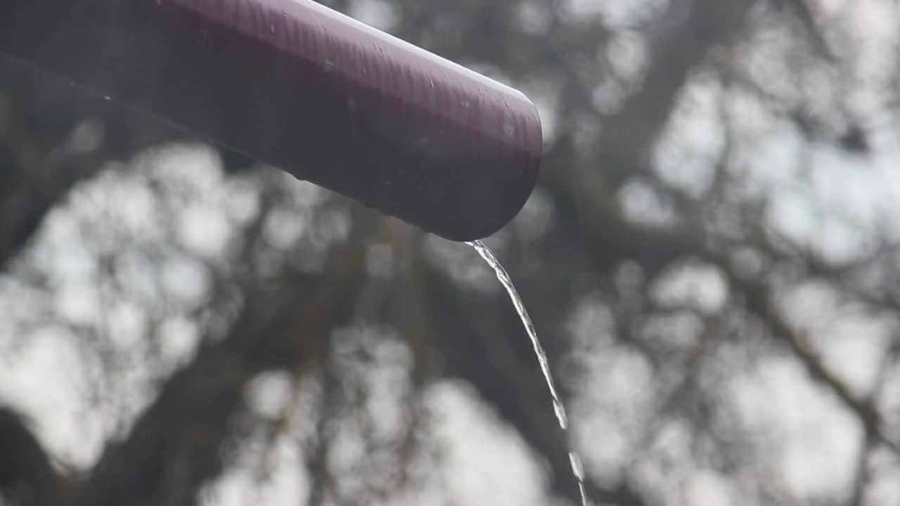 Lichte regen valt buiten het raam en een stroom water vloeit van de dakgoot naar de grond in de tuin waar het gras groeit!