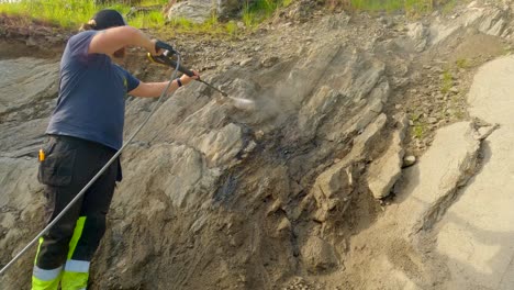 Male-clean-dirt-away-from-a-cliffside-in-the-backyard-with-a-high-pressure-washer