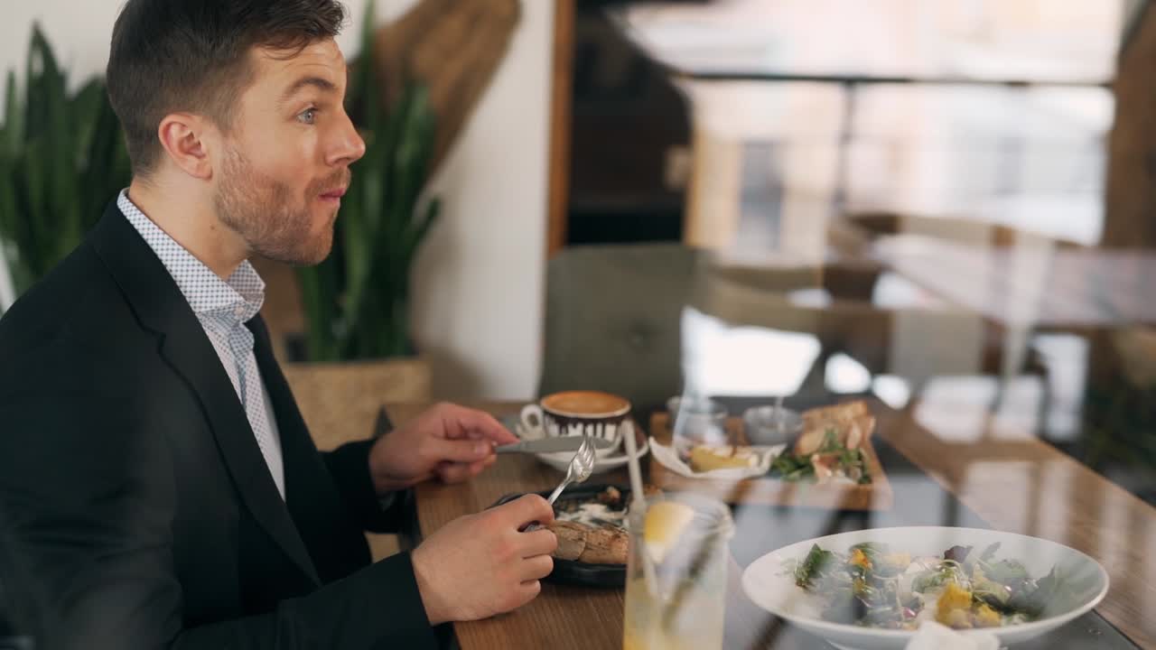 un hombre lindo y elegante disfruta de una ensalada sentada en un restaurante junto a la ventana
