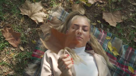 smiling female lying on plaid with dry leaf in park