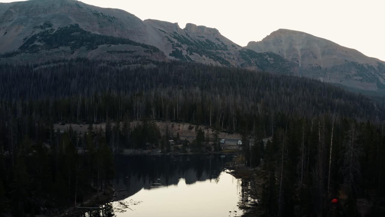 Ripresa aerea in ascesa con drone del tranquillo Lago delle Farfalle con ninfee nella Foresta Nazionale Uinta nello Utah, circondato da grandi Montagne Rocciose e pini in una nebbiosa mattina d'estate