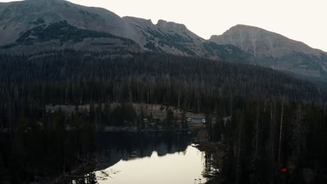 Toma-Aérea-De-Drones-Del-Tranquilo-Lago-De-Mariposas-Con-Nenúfares-En-El-Bosque-Nacional-De-Uinta-En-Utah-Con-Grandes-Montañas-Rocosas-Y-Pinos-Que-Rodean-En-Una-Mañana-De-Verano-Nublada