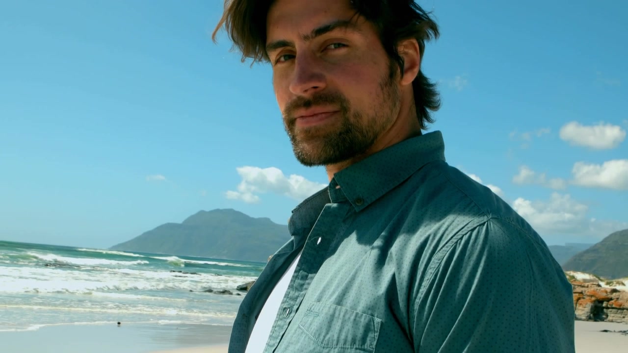 Joven de pie en la playa con el océano de fondo.