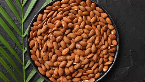 composition of whole almond nuts in black plate placed on black stone table