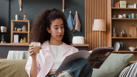 woman reading a magazine and enjoying a drink on a couch at home