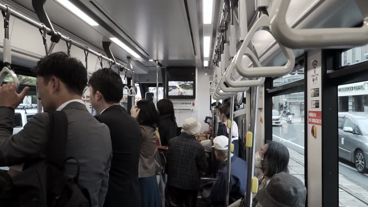View inside moving tram in Japan with old people sitting and business men standing