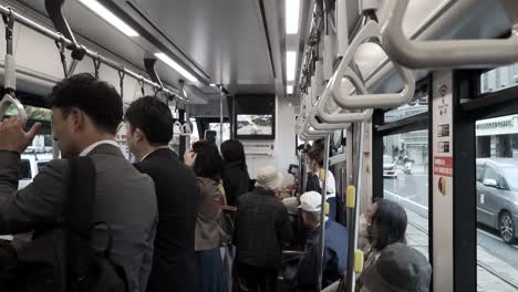 view inside moving tram in japan with old people sitting and business men standing