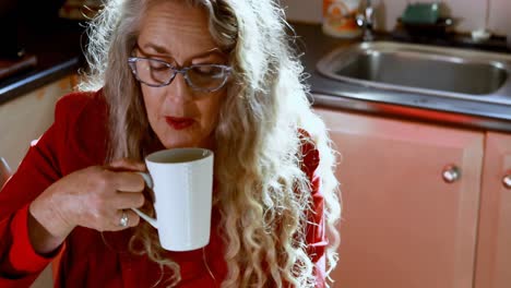 mujer madura tomando café mientras usa portátil en la cocina 4k