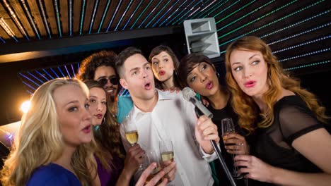 Happy-diverse-female-and-male-friends-singing-karaoke-at-bar,-holding-drinks