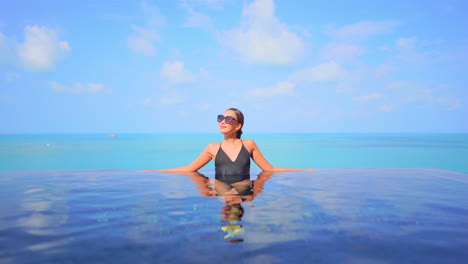 an attractive young woman leans along the edge of an infinity-edge pool with an ocean horizon in the background