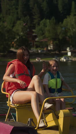 mom and daughter ride catamaran swinging on waves. woman points finger and surprised girl exclaims with amusement slow motion. active recreation in nature