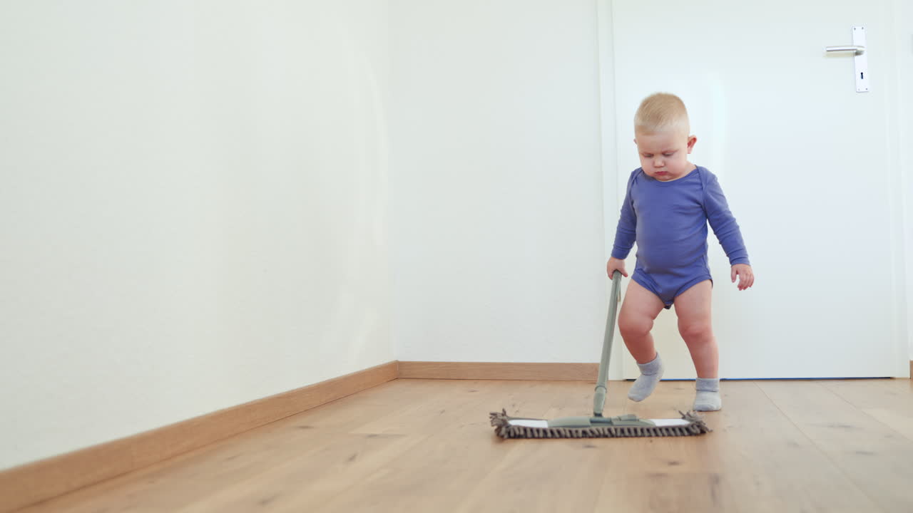 Little boy toddler washes the floor with a mop. Child helps clean the floor. Boy in a cotton bodysuit