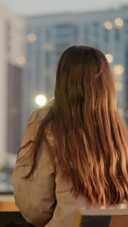 도시 공원의 벤치에 앉아있는 긴 갈색 머리카락을 가진 복아 재을 입은 여자의 뒷.