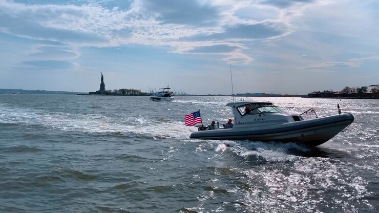 New York, USA, 8 agosto 2025: Motoscafo con bandiera americana che naviga vicino alla Statua della Libertà. Motoscafo bianco che attraversa il porto con la bandiera degli Stati Uniti che sventola e la Statua della Libertà sullo sfondo.