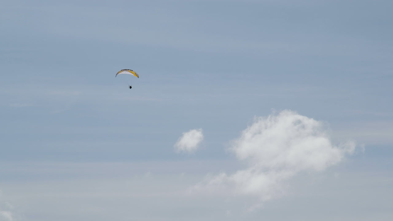 parapente motorizado que se eleva alto en el cielo azul con pocas nubes blancas, posibilidad remota