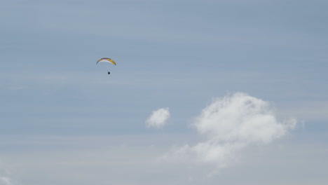 powered paraglider soaring high into blue sky with few white clouds, long shot