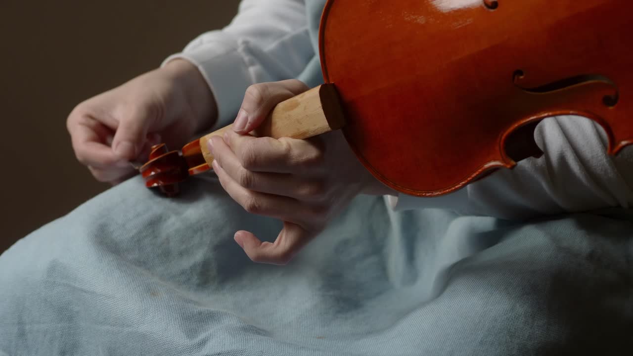 close up shot of master violin maker artisan varnishing handmade violin scroll with self produced natural paint, slow motion shot