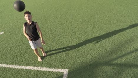 talented barefoot boy playing with soccer ball on synthetic green field, enjoying an athletic activity under bright sunlight