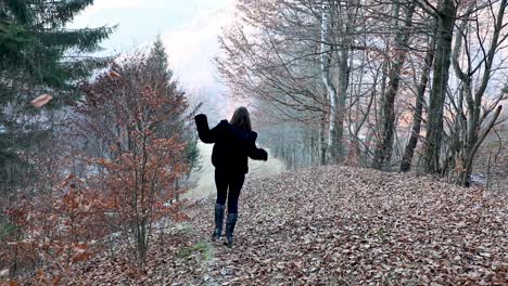 A-young-woman-happily-running-and-jumping-on-autumn-leaves-towards-trees-and-a-river