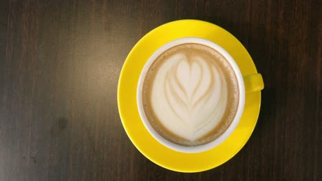 Overhead-view-of-coffee-latte-in-a-yellow-mug-and-saucer-on-a-table