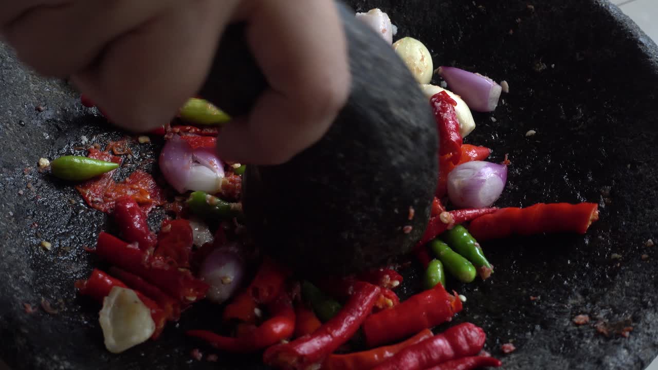 moler a mano chiles rojos y verdes, ajo y cebolla en mortero de piedra, chef preparando salsa de chile picante tradicional indonesia