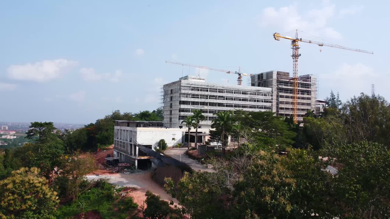 Drone descends below trees as birds fly near construction of premier hotel rebuild site in city of Ibadan, Nigeria, Africa.