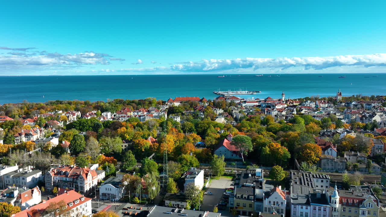 Aerial footage of Sopot city and pier area with autumn forest and ships on the horizon