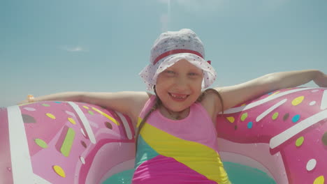 chica divertida en un anillo inflable rosa y en un divertido panamka para niños tomando el sol al sol rodando
