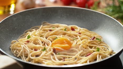 egg yolk falling into spaghetti carbonara prepared in a pan on an induction stove in a bright kitchen - slow motion