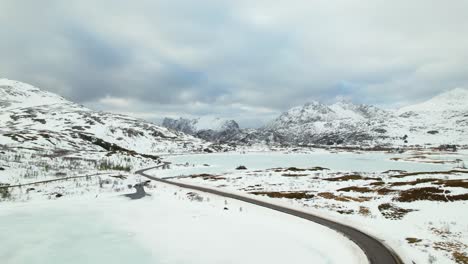 Antena-De-Camino-Sinuoso-Con-Lago-Congelado-Y-Montañas-Cubiertas-De-Nieve---Drone-4k