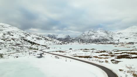 Aerial-of-winding-road-with-frozen-lake-and-snow-covered-mountains---Drone-4k