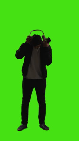 Vertical-Video-Full-Length-Shot-Of-Man-Wearing-Wireless-Headphones-Streaming-Music-From-Mobile-Phone-Against-Green-Screen-2