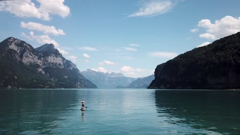 Orbiting-aerial-shot-around-a-stand-up-paddler-on-a-yellow-stand-up-paddle,-sup-with-a-straw-hat-in-the-middle-of-a-lake-in-Switzerland