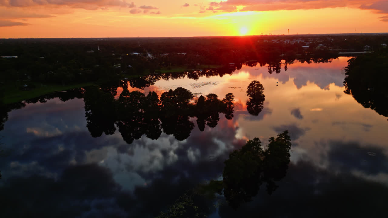 Orange glow over water and forest line, perfect reflection during vivid tropical sunset, aerial pullback
