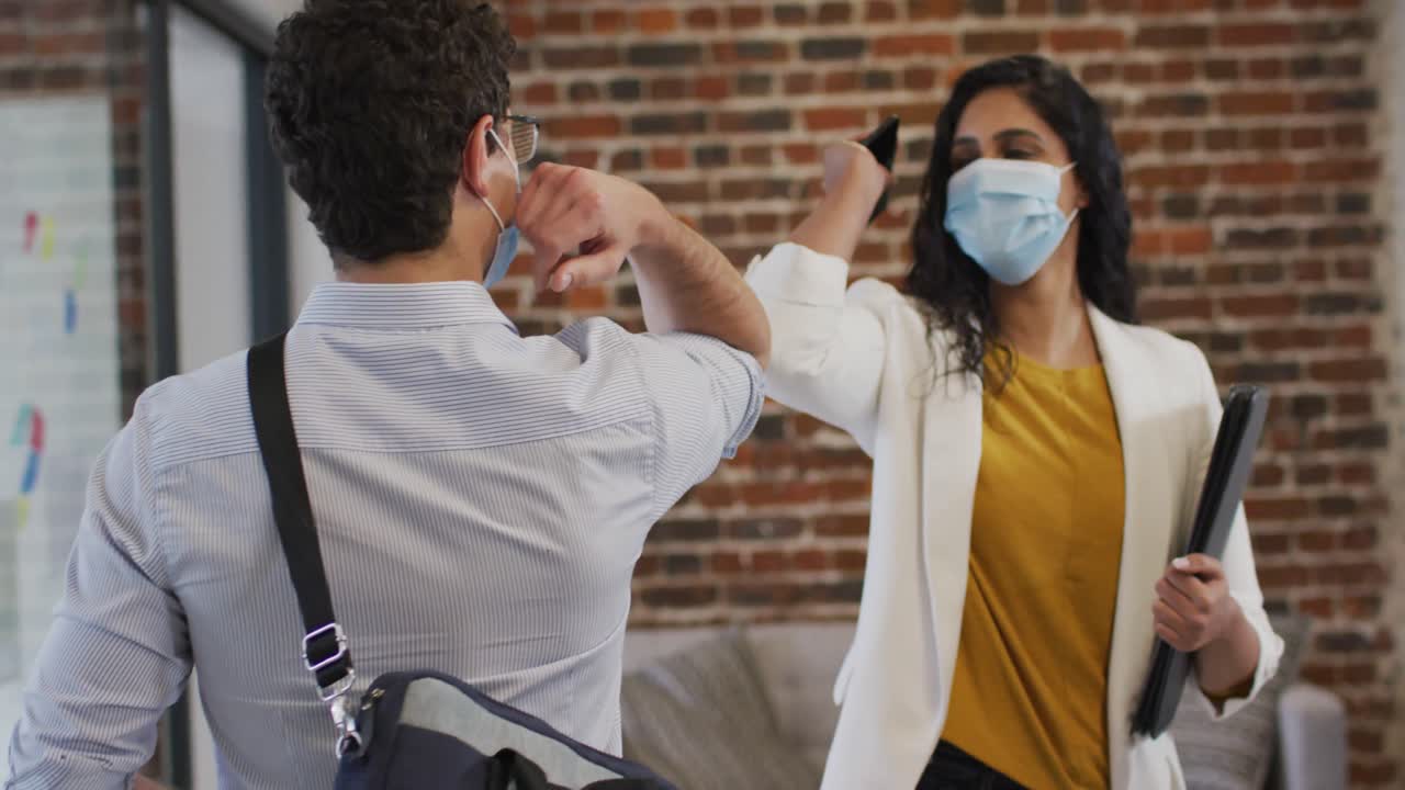 мужчина и женщина в масках приветствуют друг друга, касаясь локтей в офисе