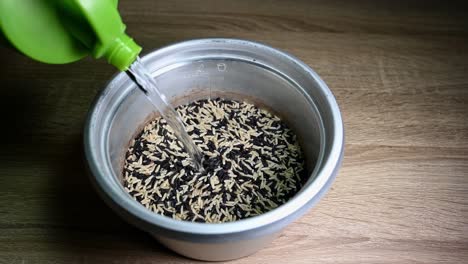 rice cooker with some rice and water is added poured from a green container and then to be cooked