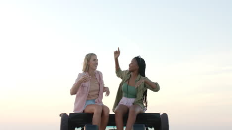 young african american woman and young caucasian woman sit atop a vehicle outdoors on a road trip