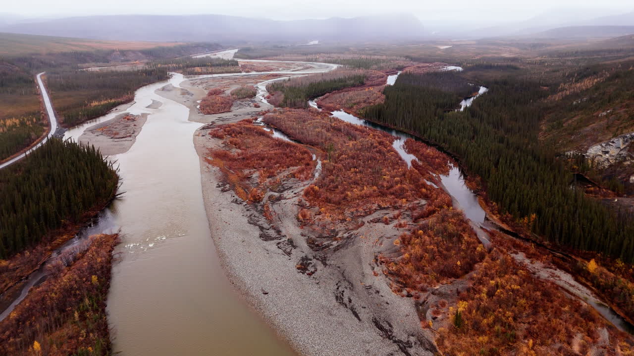 Ogilvie River Flowing Along The Dempster Highway, Mountain And Forest During Autumn On A Foggy Morning In Yukon, Canada. - aerial shot