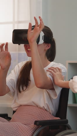 blonde woman touches arm of friend with disability in vr goggles laughing. lady sits in wheelchair experiencing virtual reality games at home closeup