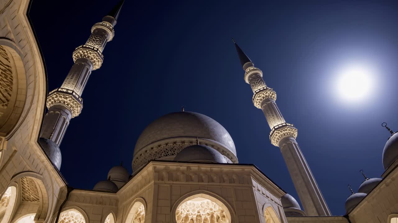 Una ripresa video da un'angolazione bassa di una moschea di notte, che mette in risalto le sue cupole e i minareti sotto una luce brillante.